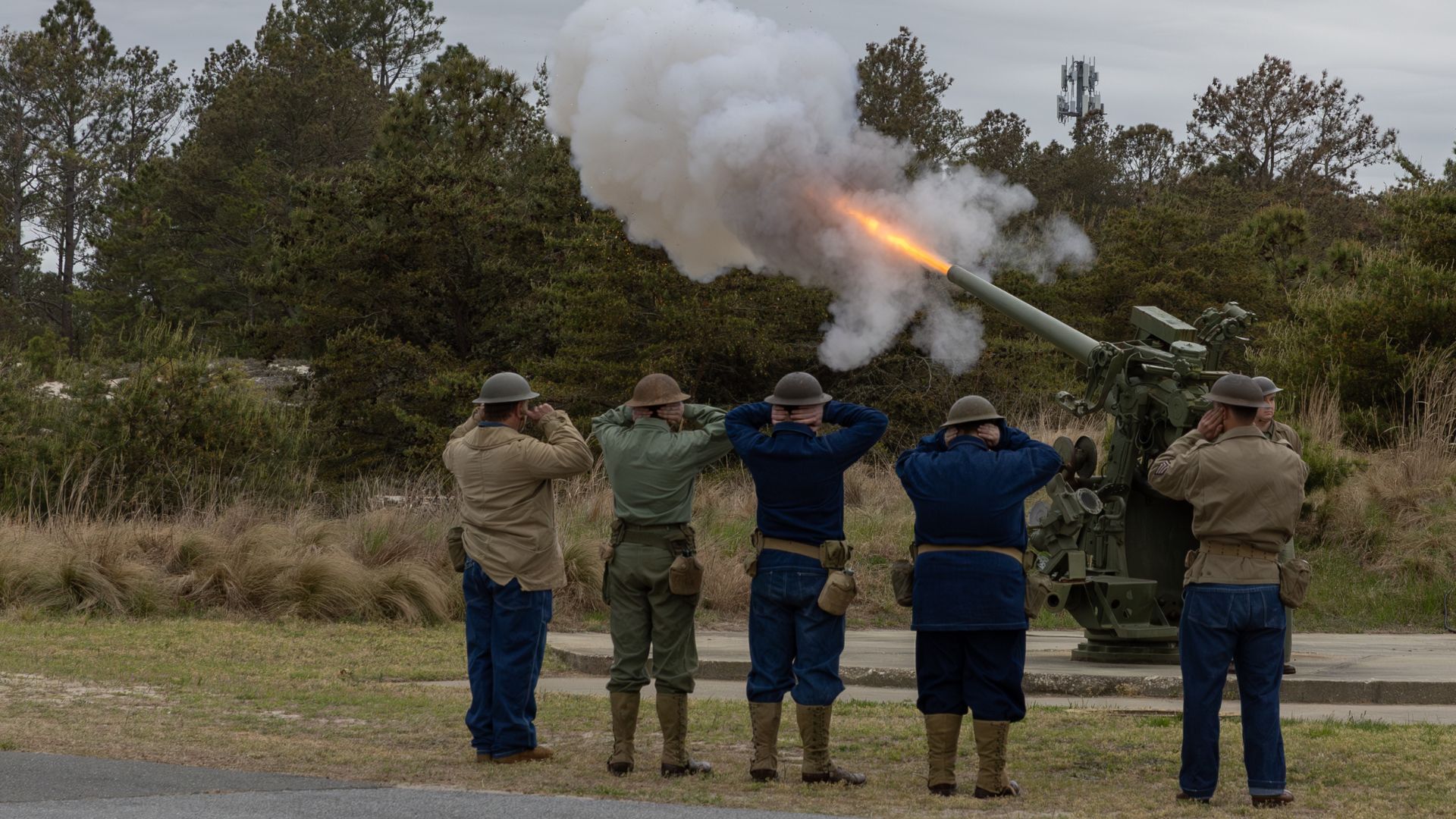 A crew of soldiers firing a field artillery gun, with flame and smoke erupting from the muzzle.