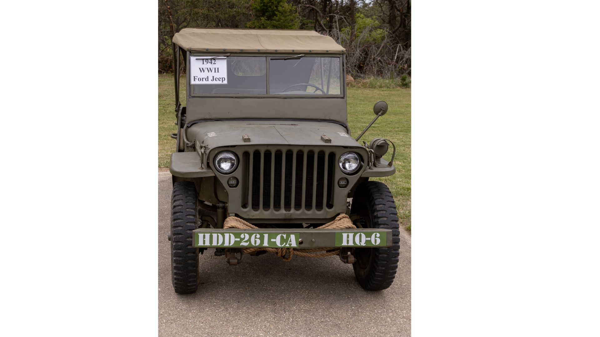 Front view of a WWII-era olive-drab 1942 Ford Jeep with a canvas top and a sign in the windshield reading '1942 WWII Ford Jeep'