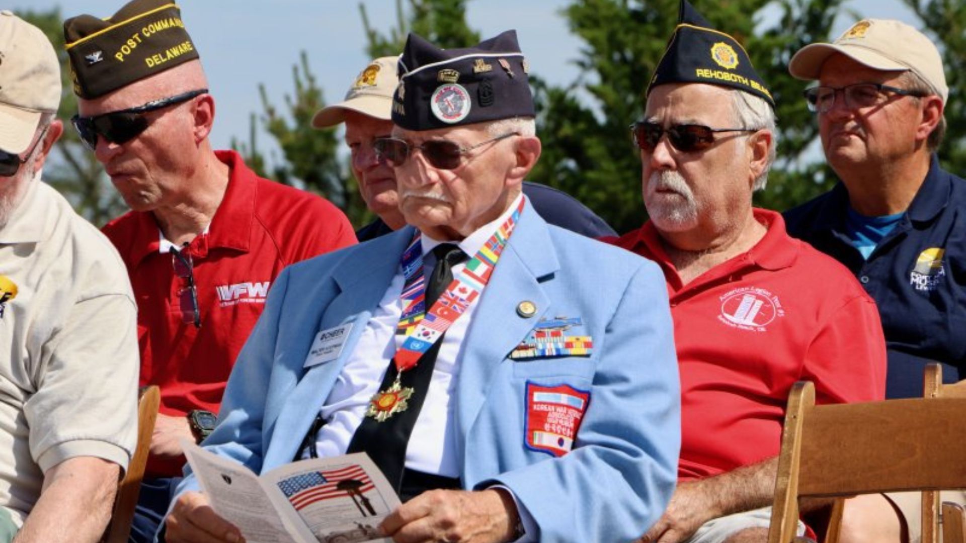 Group of elderly veterans in colorful jackets and hats, sitting outdoors and reading a flyer together