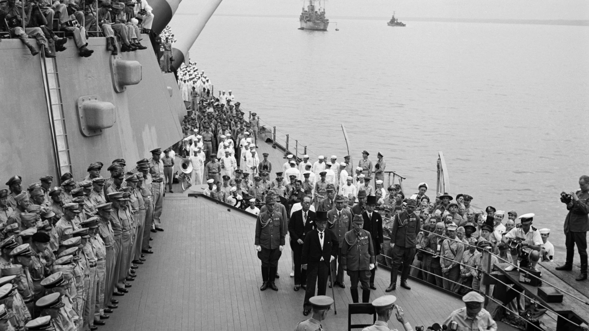 Crew and officers stand in formation on a ship's deck during a formal ceremony at sea.